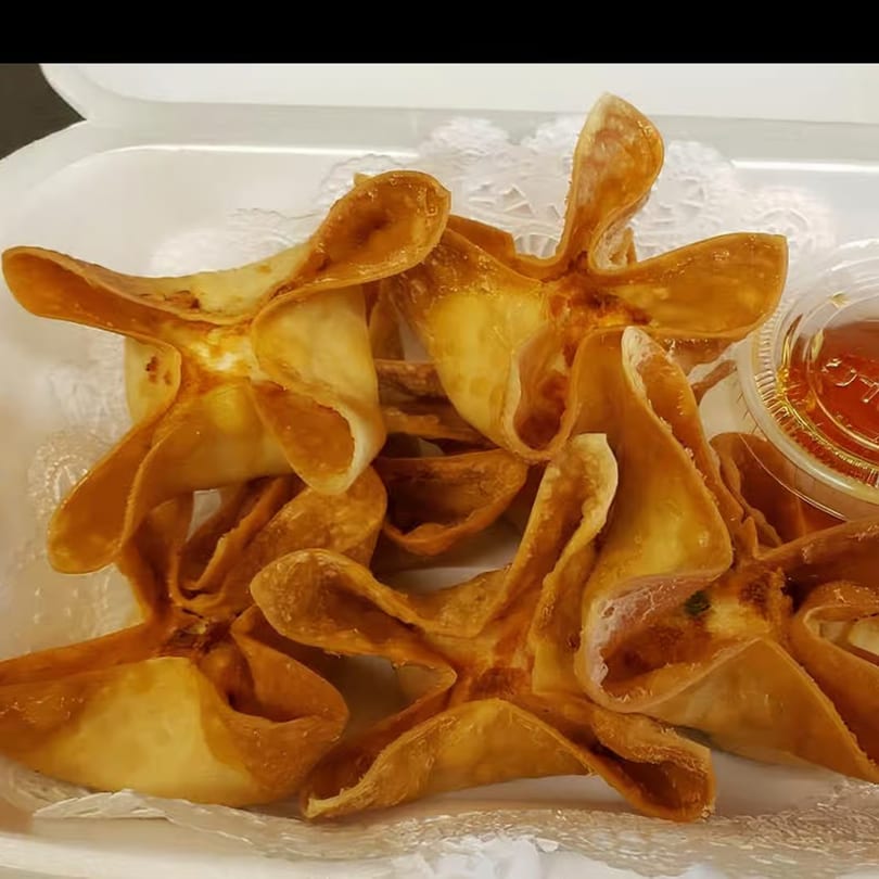 Golden-brown crab rangoon in a white takeout container with a side of dipping sauce.