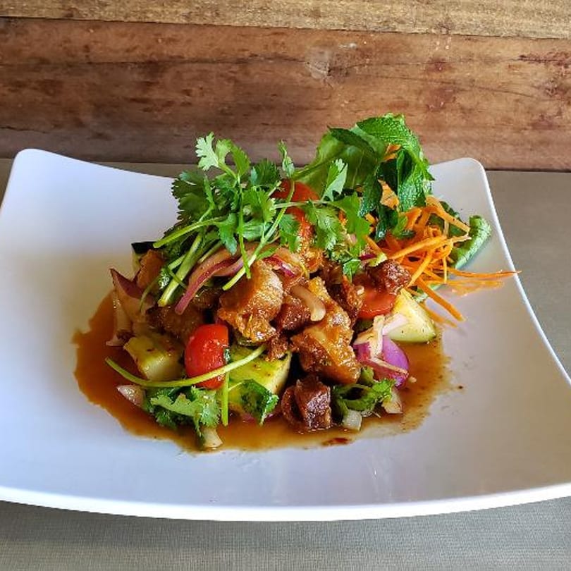 Thai salad with crispy pork, fresh herbs, red onions, and tomatoes on a white plate.