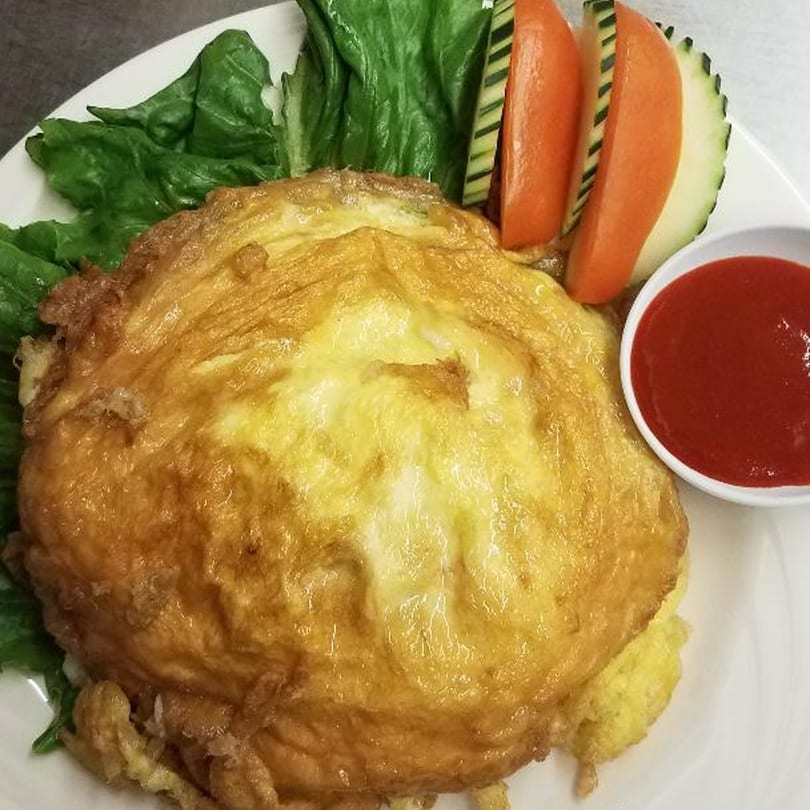 Crispy Thai omelet with lettuce, cucumber, tomato slices, and a side of red sauce.