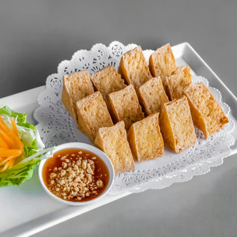 Crispy fried tofu triangles with a side of peanut dipping sauce and fresh lettuce.