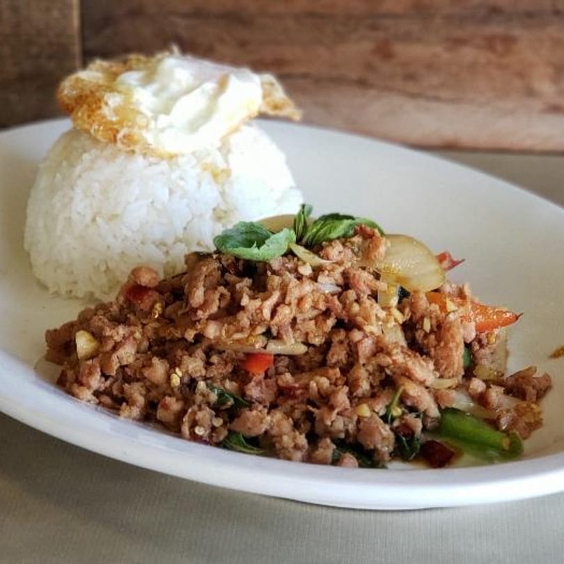 Thai basil chicken with rice and a fried egg on a white plate.