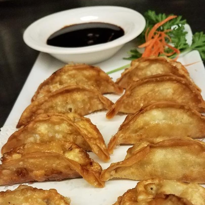 Crispy golden-brown Thai dumplings arranged on a white plate with a side of dark dipping sauce.